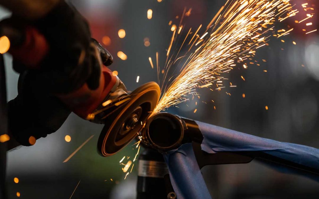 Worker cutting, grinding and polishing motorcycle metal part with sparks indoor workshop, close-up. Advantages of working with a professional welding company