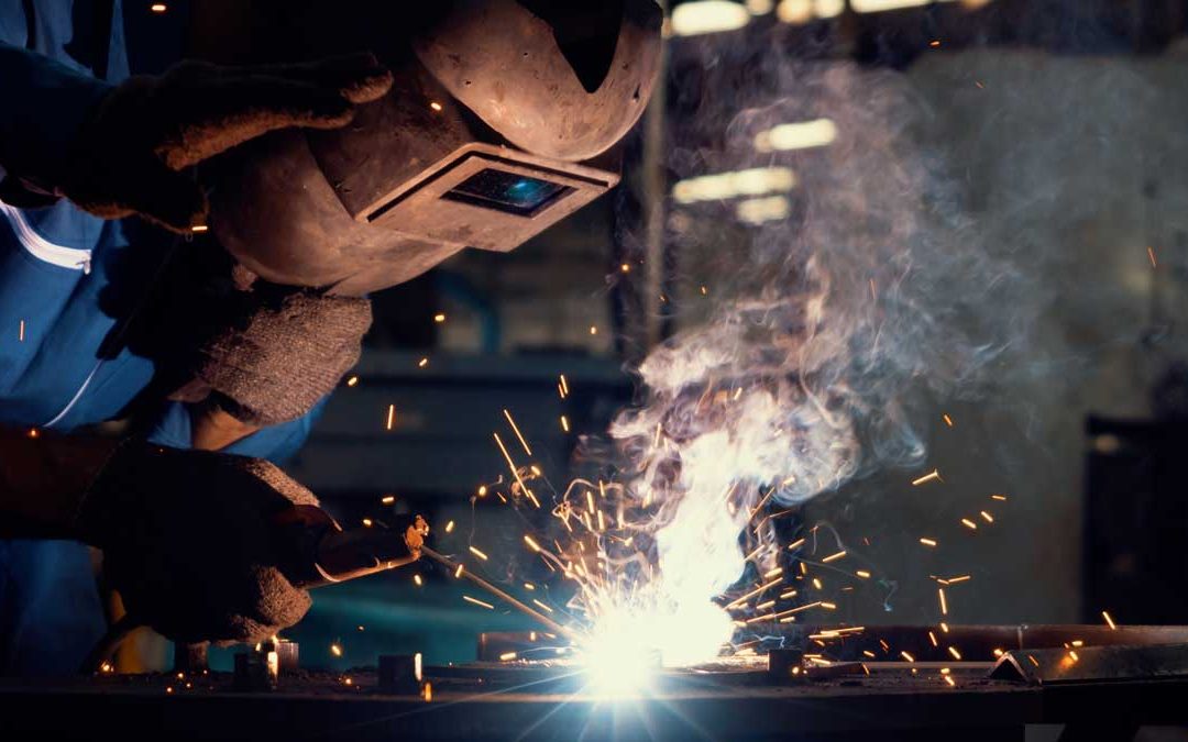 How does welding work? Skillful metal worker working with arc welding machine in factory while wearing safety equipment.